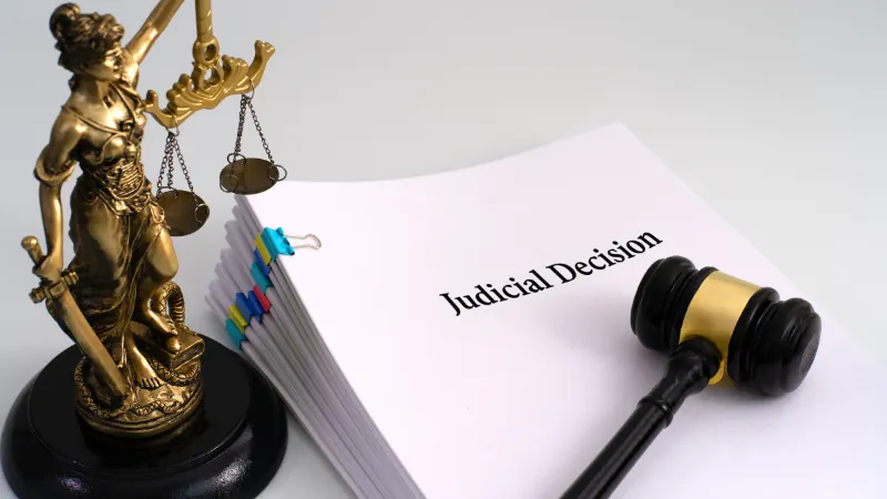 A Lady Justice statue beside a stack of documents titled 'Judicial Decision,' with a gavel resting on top